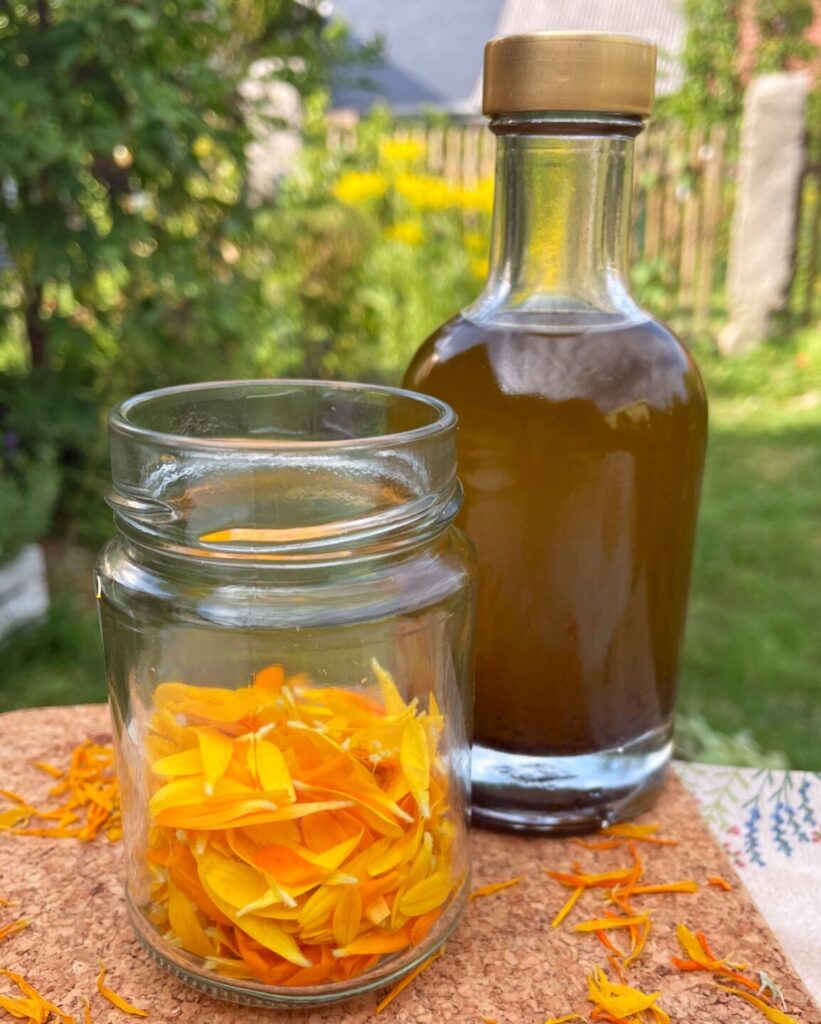 Glas mit Ringelblumenblüten und eine Flasche Olivenöl